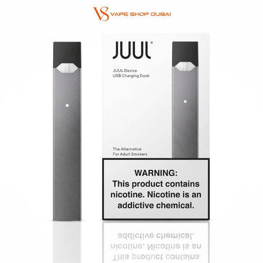 A JUUL disposable vape device and its USB charging dock packaging are shown on a white background, with a prominent nicotine warning label in front. The JUUL Shop Dubai brand logo is visible at the top.